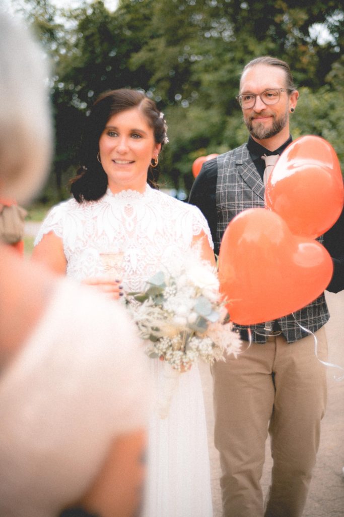 Ehepaar glücklich Nina Hübner Hochzeitsplanung Göttingen Braut mit Blumenstrauß und Herzen, im Hintergrund ein Mann im Anzug.