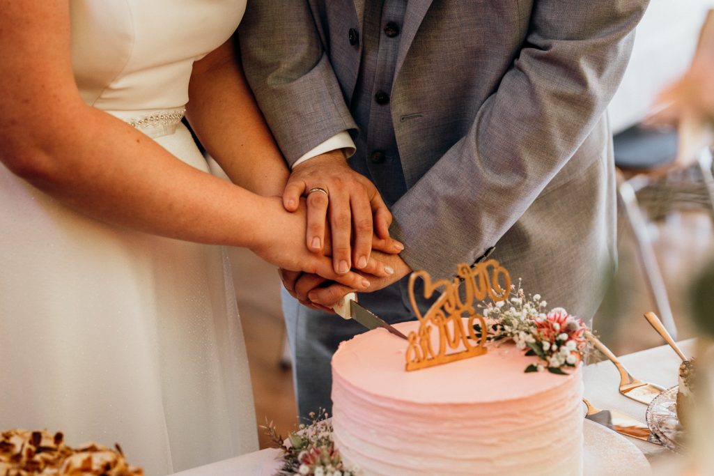 Hochzeitsplanung von Nina Hübner Göttingen Hochzeitskuchen mit zwei Händen, die sich über den Kuchen legen, dekoriert mit Blumen.