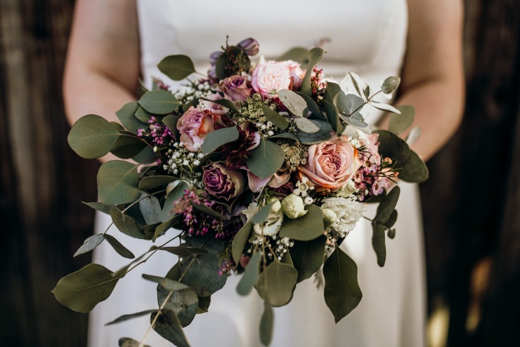 Hochzeitsstrauß aus rosa und lila Blumen mit grünen Blättern.